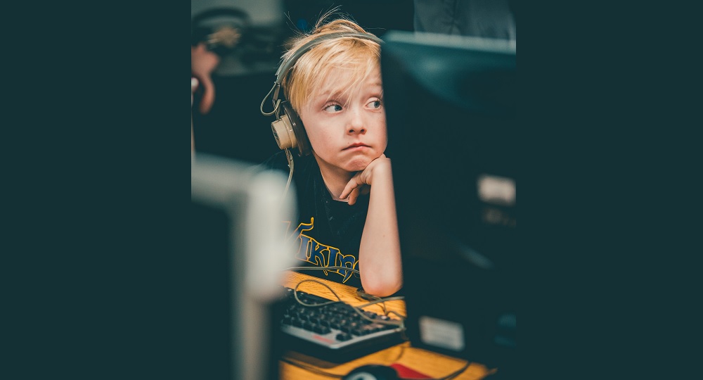 remote: Unhappy blond child wearing headphones looks away from computer