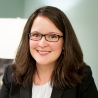 Naomi Smoot Evans (headshot), executive director of Coalition for Juvenile Justice, smiling woman with shoulder-length brown hair, glasses, earrings, patterned scarf, dark suit.