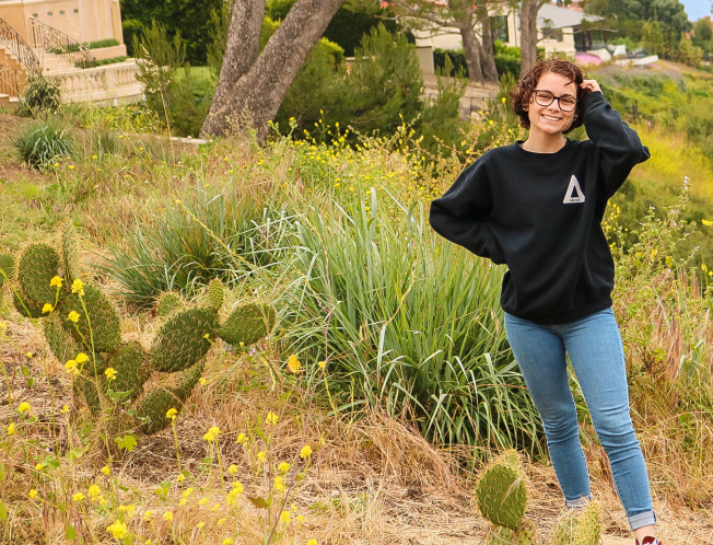 alt text: mental health: smiling woman in glasses, sweatshirt, jeans standing outside among cacti