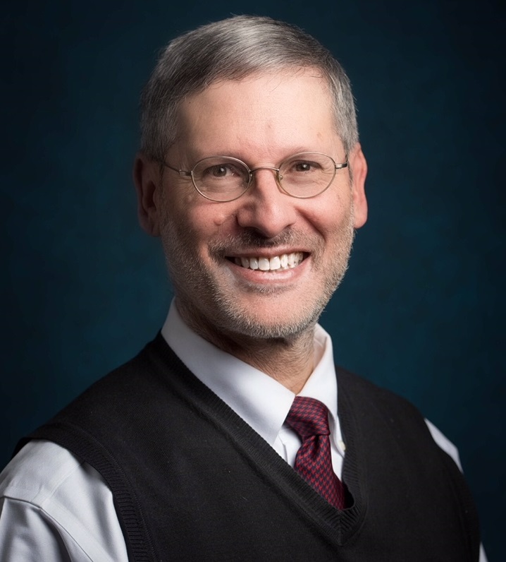peer-on-peer: Daniel Pollack (headshot), Yeshiva University professor; smiling man with beard, mustache, glasses wearing blue tie, white shirt, dark vest.