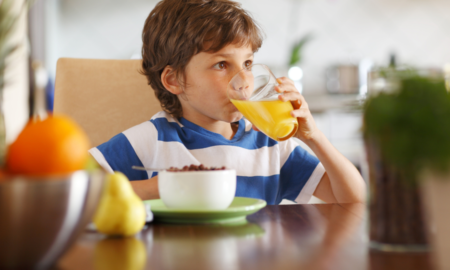 Child Care and Feeding Young Children During Pandemic report; young boy drinking orange juice with bowl of food on table