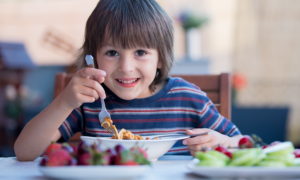 Grants for improving nutrition of households on food assistance programs: Cute child, preschool boy, eating spaghetti for lunch outdoors in garden, summertime