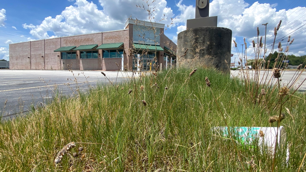 Grass growing around empty parking lot around closed large building.