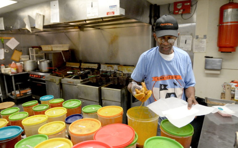 Macon: Man in ball cap, T-shirt dunking something in plastic tub in commercial kitchen.