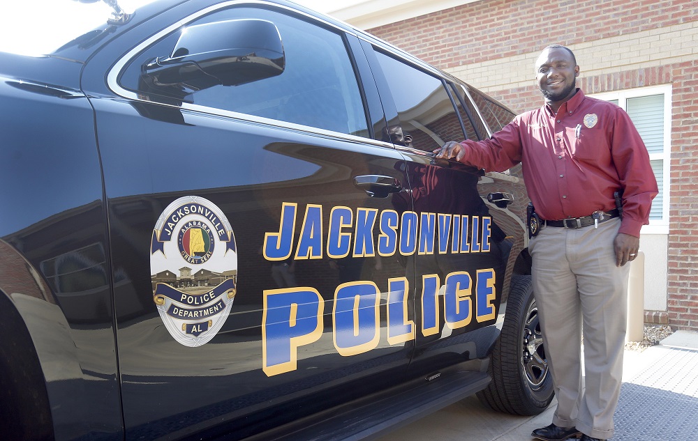 police: smiling man with red shirt, khaki pants leans on SUV labelled Jacksonville Police