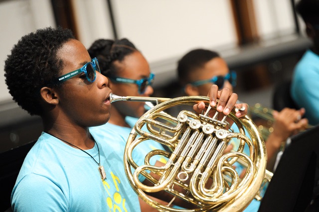 Miami: Line of students play instruments wearing blue sunglasses, uniform T-shirts