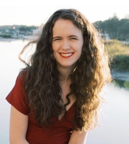 telemedicine: smiling woman with long brown curly hair wearing maroon top in front of lake