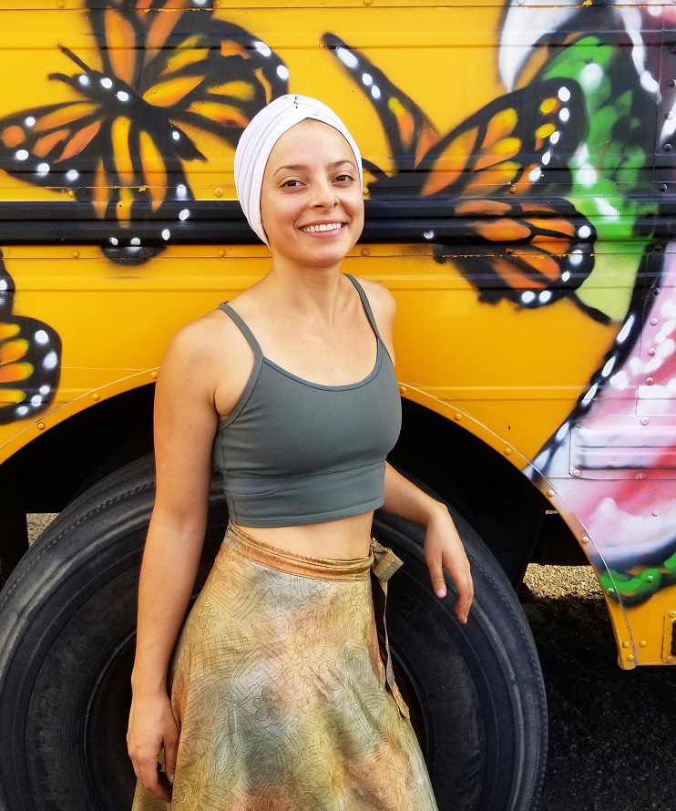 support: Smiling woman in headscarf in front of school bus with mural on it.