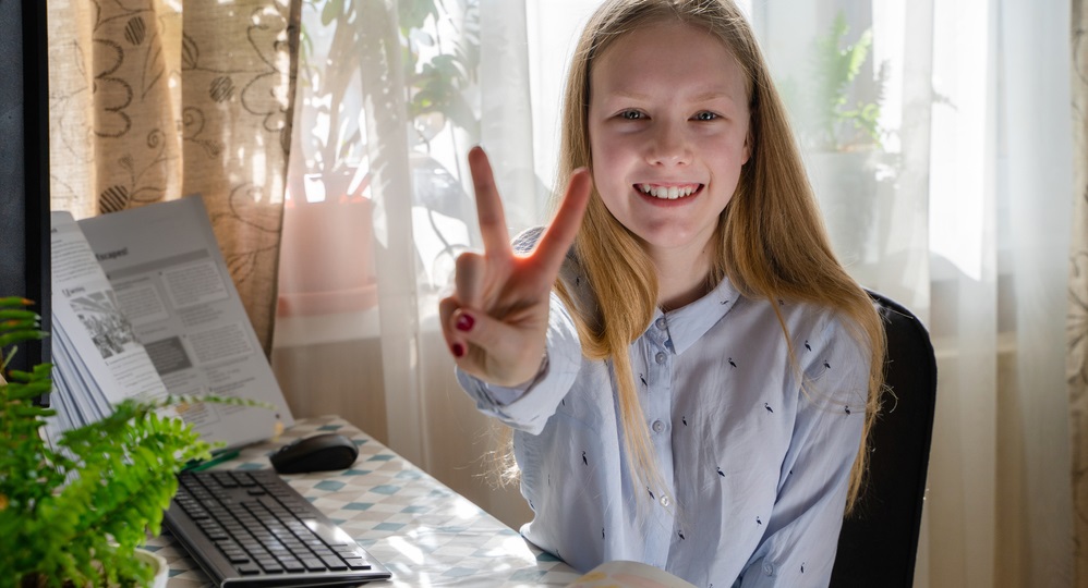 support: Smiling girl with long blond hair makes peace sign with fingers.