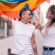 Breaking Barriers to Quality Mental Health Care for LGBTQ Youth report; Lesbian couple with playful attitude showing proudly a pride lgbt flag.