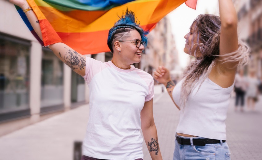 LGBTQ+ community; Lesbian couple with playful attitude showing proudly a pride lgbt flag.