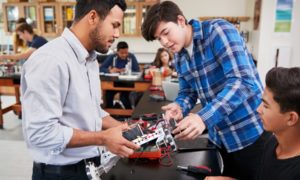STEM education grant; Teacher With Male Pupils Building Robotic Vehicle In Science Lesson
