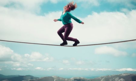 positive psychology: Woman balancing on a rope above clouds and mountains while listening on headphones