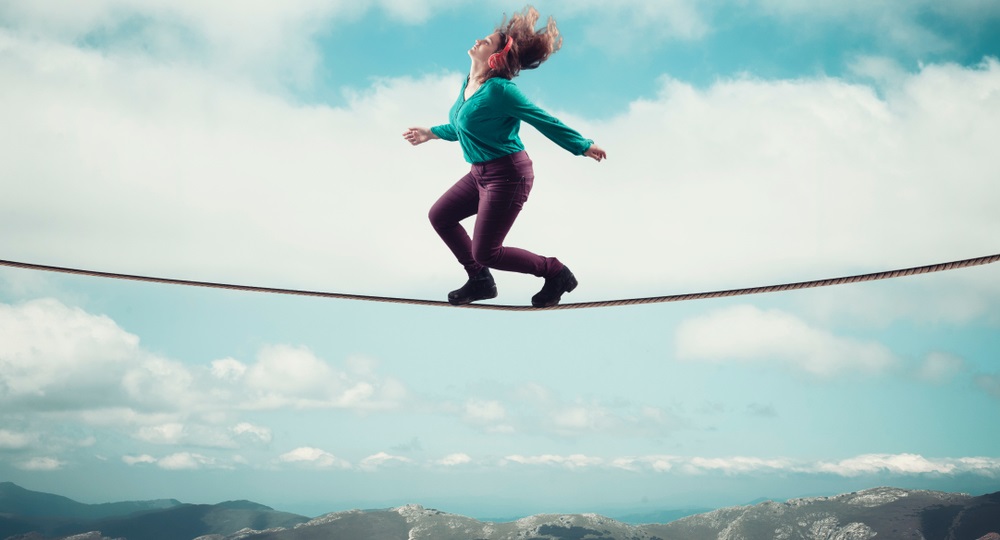 positive psychology: Woman balancing on a rope above clouds and mountains while listening on headphones