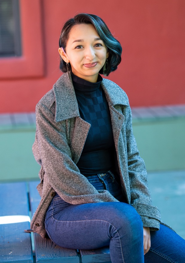 accessibility: smiling woman with blue top, blue jeans and gray jacket sitting on steps outside