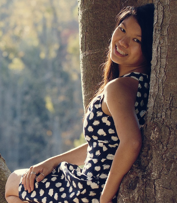 travel: Woman wearing black and white dress with long brown hair poses curled up in tree