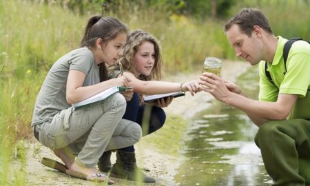 K-12 environmental education: two female students work with teacher on water quality outdoors