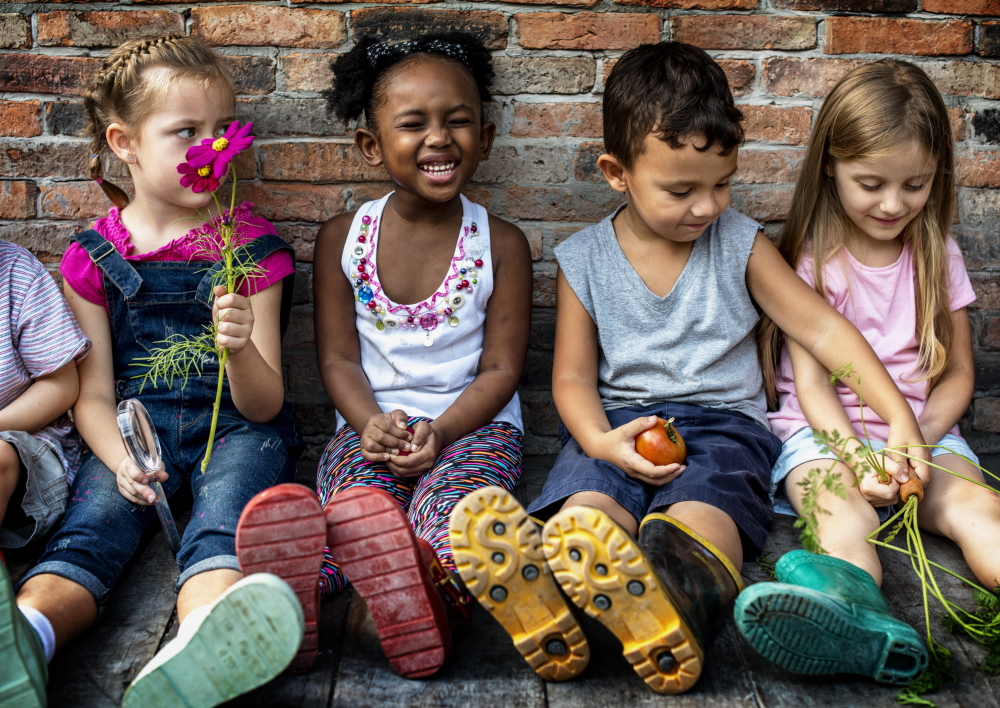 Group of smiling small kids sit against brick wall