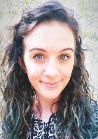 smiling woman with long curly brown hair partly dyed green wearing black and leopard print top
