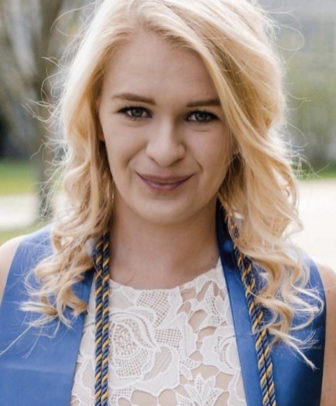 smiling woman with long curly blond hair wearing sleeveless blue top with lace insert