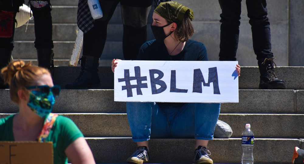 protests: White woman sits on steps holding #blm sign