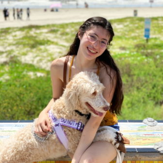 stimulus: smiling woman with glasses, long brown hair, tank top sits outside with dog in her lap