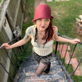 Woman with maroon hat, red hair, patterned tights posing on stairs 
