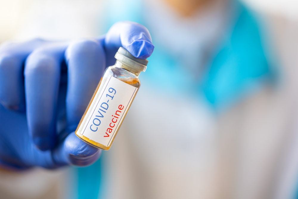 Person in blue gloves holding vial with COVID-19 vaccine written on it