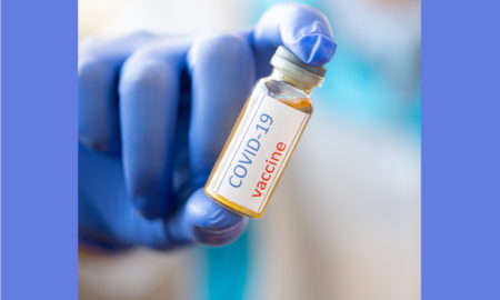Person in blue gloves holding vial with COVID-19 vaccine written on it