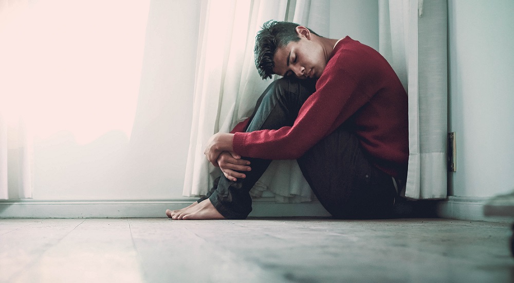 suicide: Youth sitting on floor next to curtain, head on knees