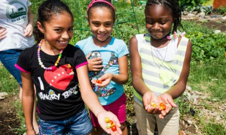 community healthy food access and healthy living through COVID grants; three young girls holding fresh tomatoes and smiling