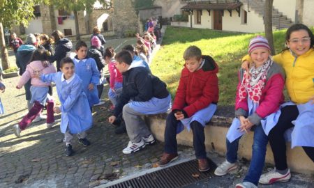 community: Kids in jackets sit outside their school, goof off.