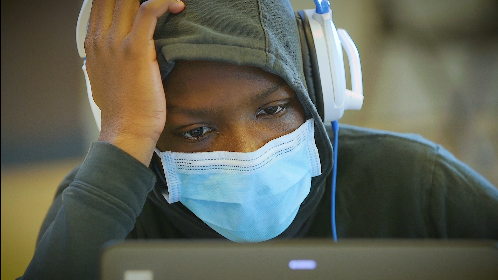 homelessness animation: Close-up of student in mask, hoodie, headphones leans over laptop