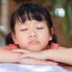 afterschool: Little girl with closed eyes rests chin on arms on table.