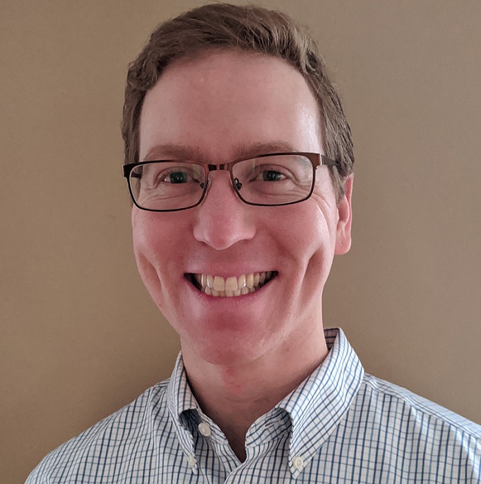 gun violence: Sean E. Snyder (headshot), licensed clinical worker, smiling man with short brown hair, very deep twin dimples in cheeks, glasses and light blue plaid shirt.