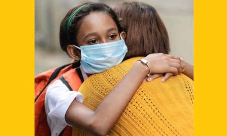 Kids, Families, and COVID-19 report cover; sad looking girl with medical facemask on hugging someone