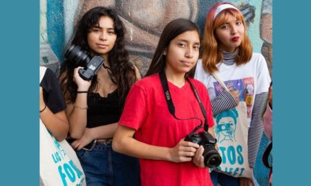 Latinz Arts/Culture support grants; three young Latin female photographers pose for picture in front of painted wall mural