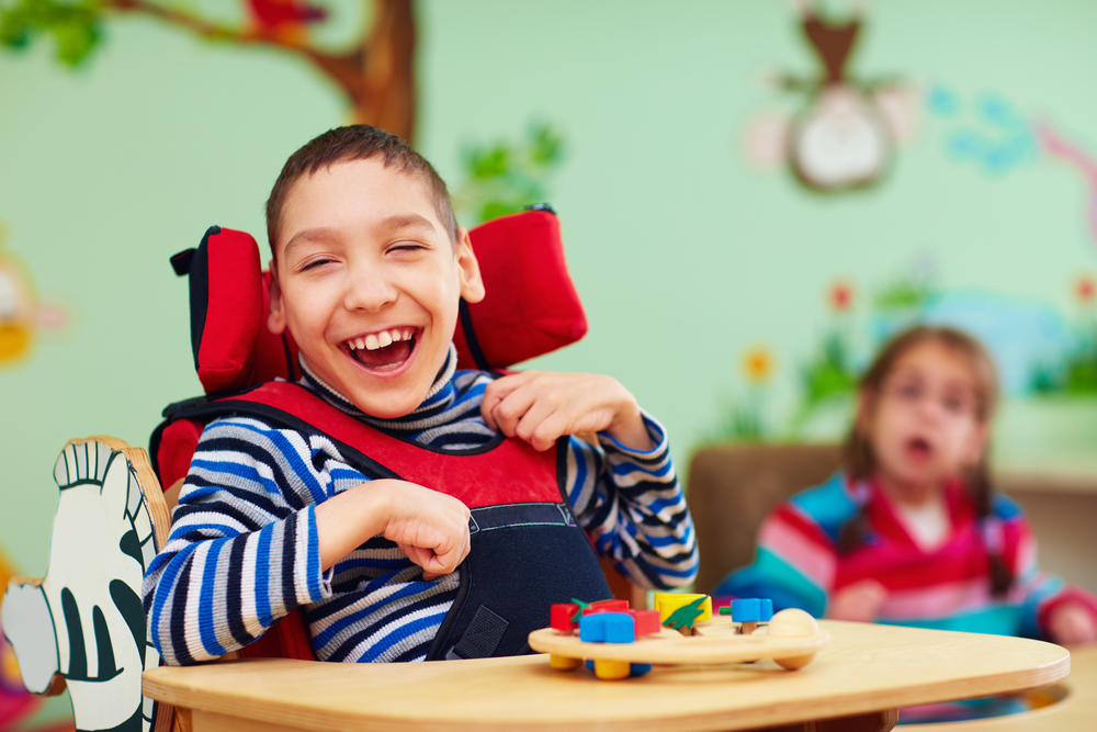 disability: cheerful boy with disability in chair with tray in front of him with toy