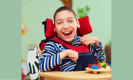 disability: cheerful boy with disability in chair with tray in front of him with toy