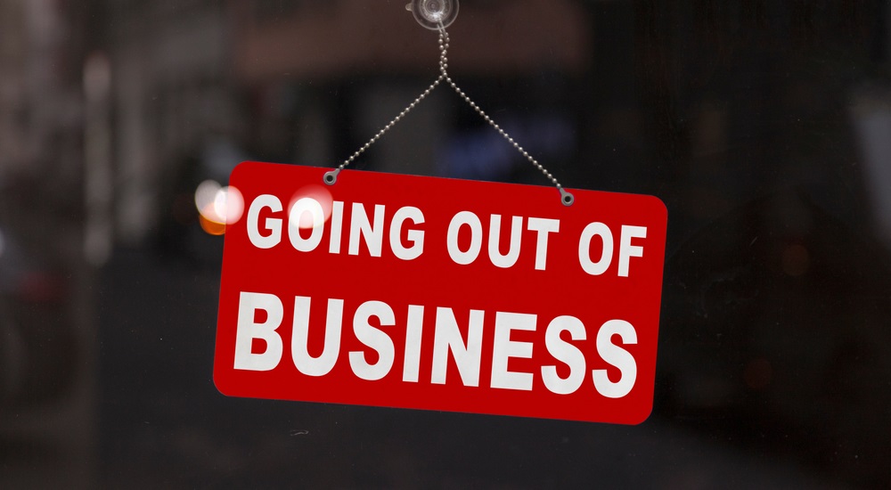 jobs: Close-up on a red closed sign in the window of a shop displaying the message Going out of business.