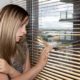 mandated reporter: Young woman wearing a summer dress looks concerned while looking out the window blinds