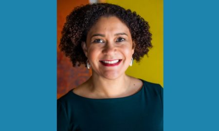 Elizabeth Lindsey newsmaker headshot; african american woman with curly hair and earings in dark blue shirt on orange background