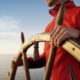 Boat navigator holding wooden wheel wearing red jacket with ocean horizon background