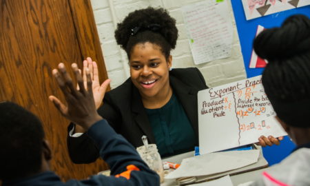 tutoring: Smiling woman holding sign with math instructions high-fives a child.