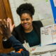 tutoring: Smiling woman holding sign with math instructions high-fives a child.