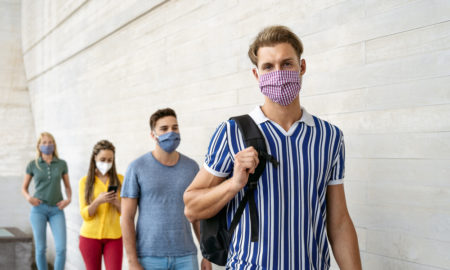 students not returning to school: young adultstudents lined up 6 feet apart wearing masks standing in front of cream brick wall