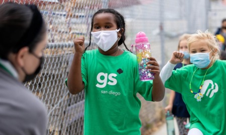 San Diego region summer learning: two young girls in green shirts and white facemasks happily running with water bottles