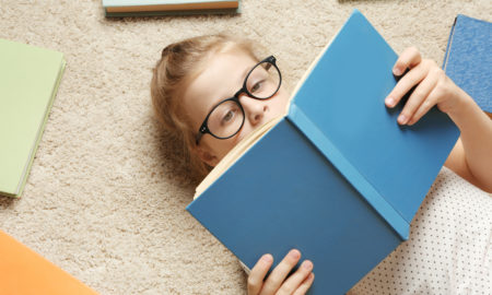 story county reads: young girl with blond hair and dark glasses reading blue book