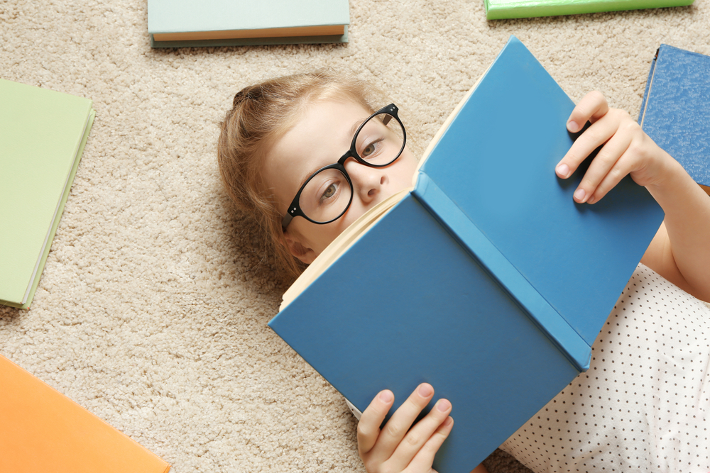 story county reads: young girl with blond hair and dark glasses reading blue book