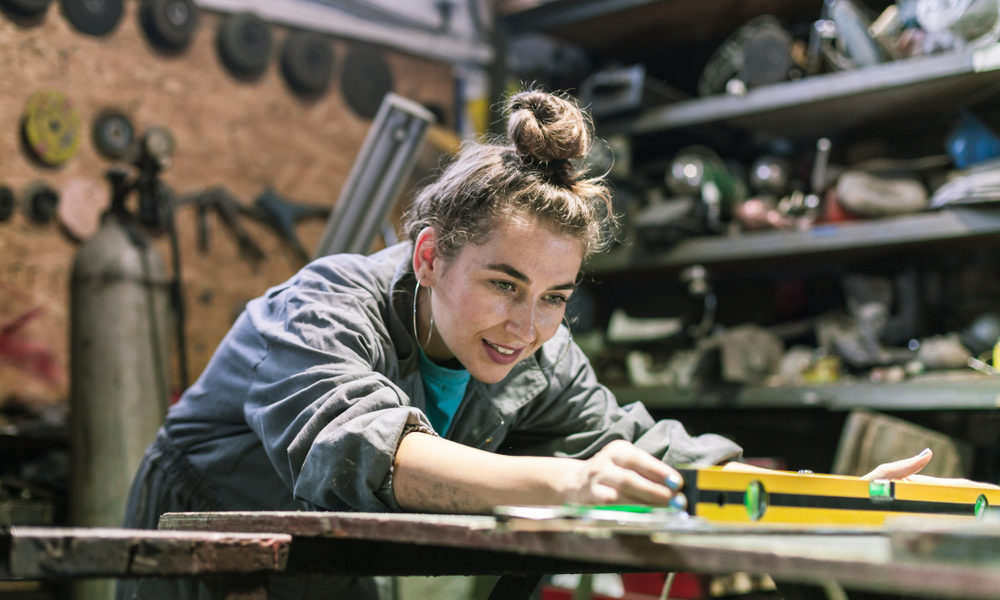 skilled trades and trades education: Yong person with brown hair in top knot leans over work tale peering at liquid in long yellow level